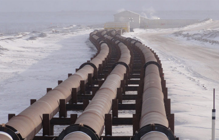 Large gray pipes in black brackets used in the oil sands industry surrounded by snow